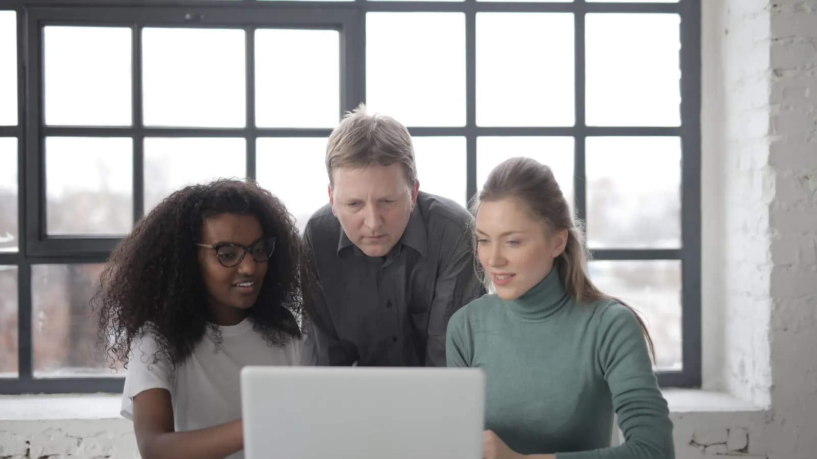 Trois personnes d'une petite équipe regardent ensemble l'écran d'un ordinateur portable