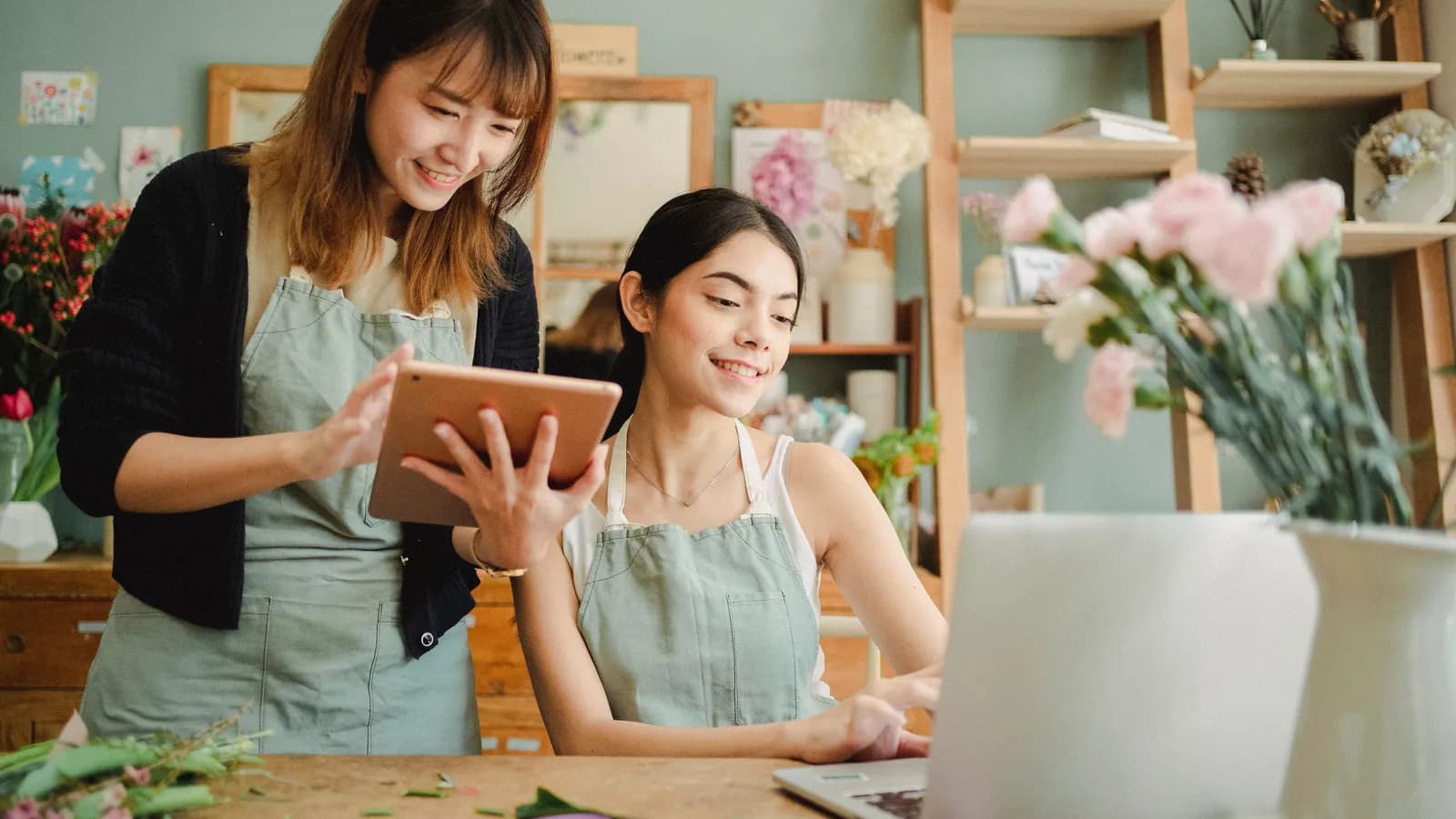 Deux commerçantes d'un petit magasin regardent ensemble une tablette et un ordinateur portable