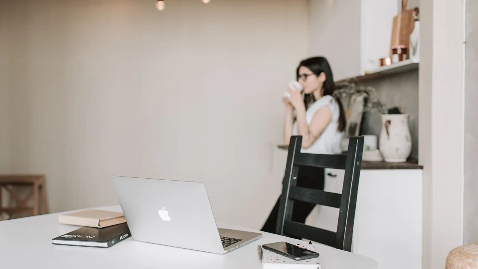 Un ordinateur portable ouvert sur un bureau pendant qu'une personne fait une pause café en arrière-plan