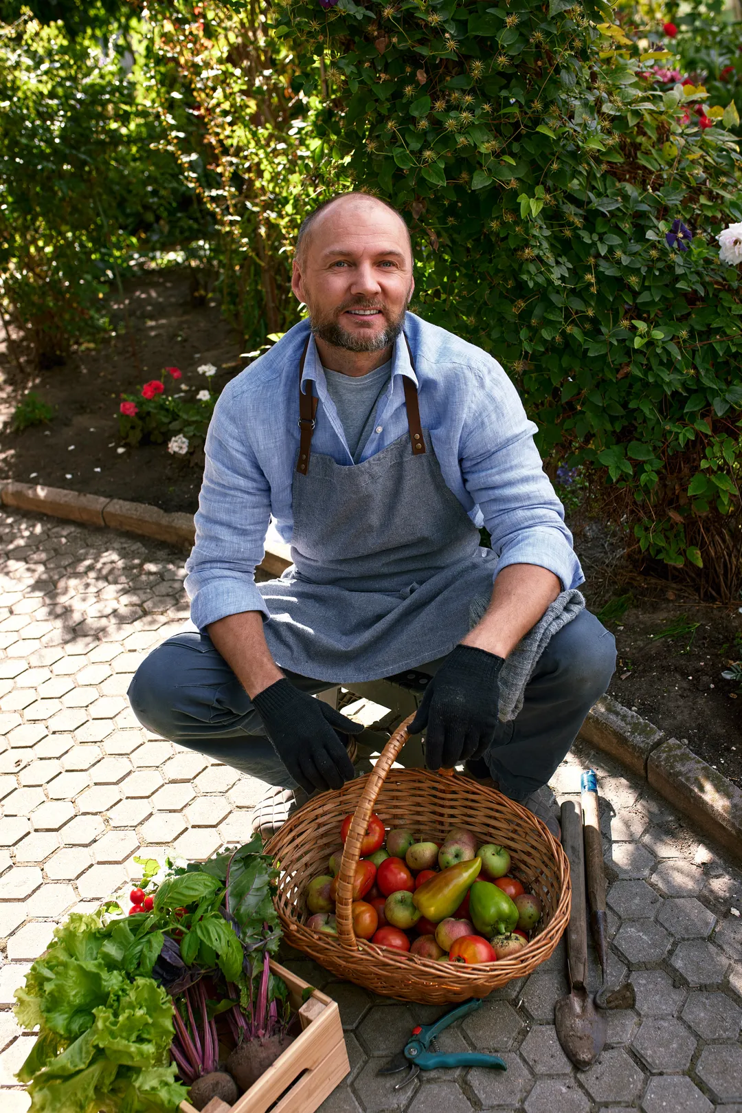 Producteur accroupi près d'un panier de tomates et d'une cagette de légumes
