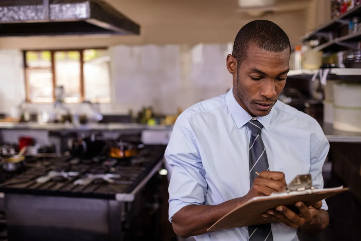 Inspecteur prenant des notes sur un clipboard dans une cuisine de restaurant